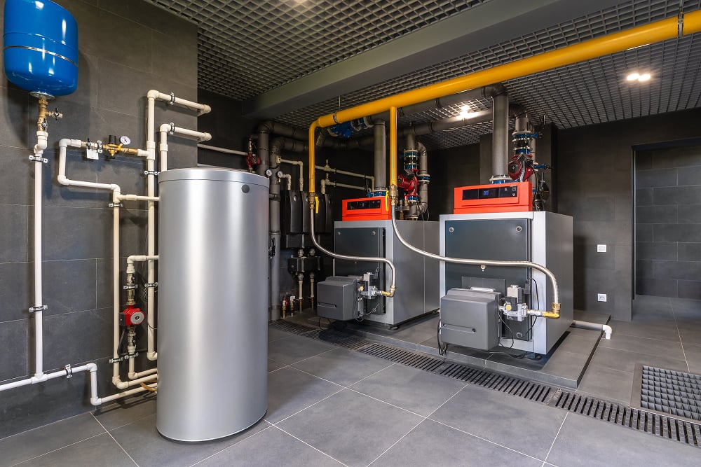 Modern boiler room with two large metal boilers, pipes, and a storage tank. The room is well-organized, with a sleek, industrial appearance.