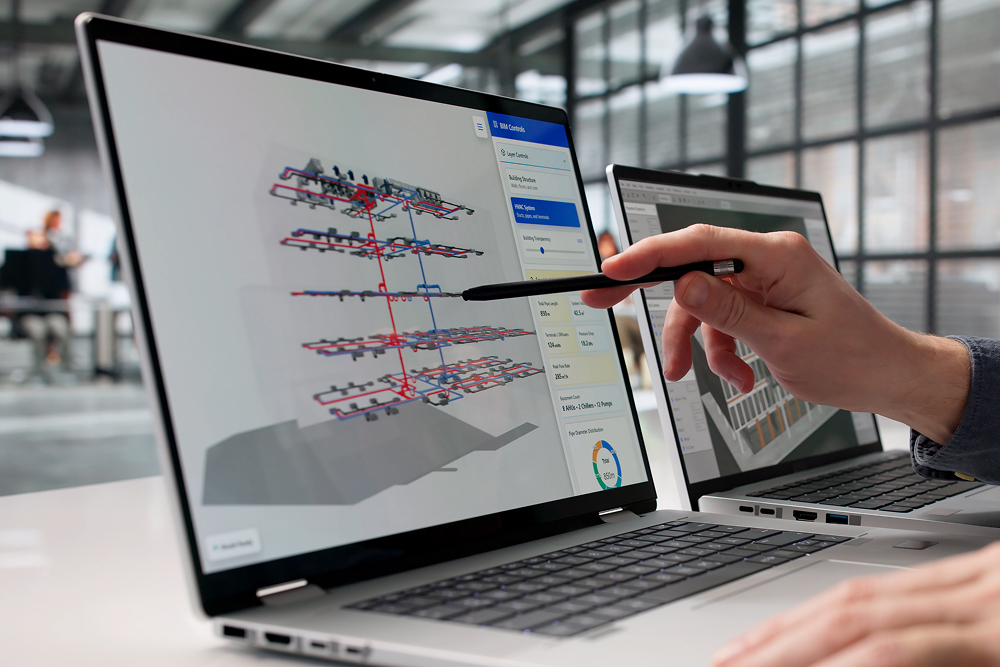Person points a pen at a laptop screen showing a 3D architectural model with layered designs. Modern office setting with another laptop in view.
